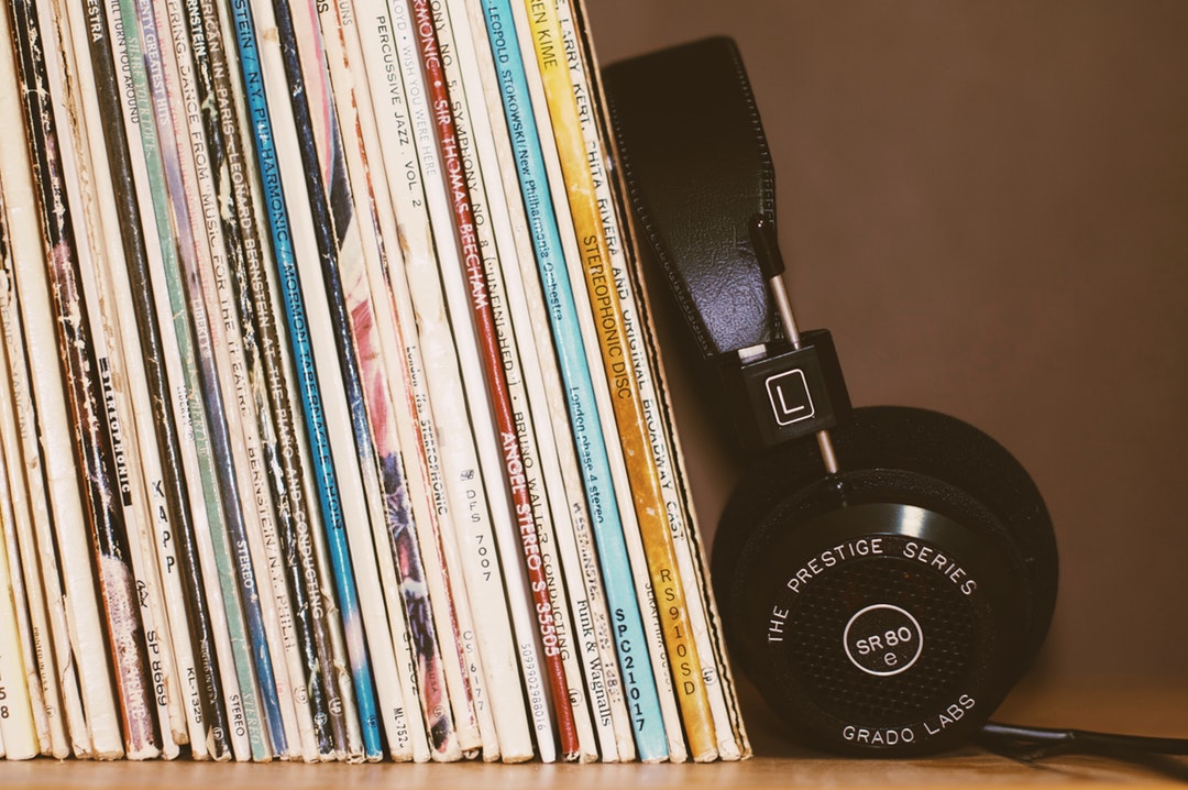 Black headphones leaning against a collection of vinyl records on a shelf