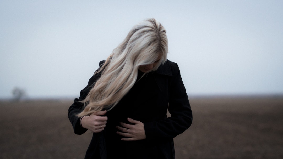 Person with long blonde hair buttoning their coat outside
