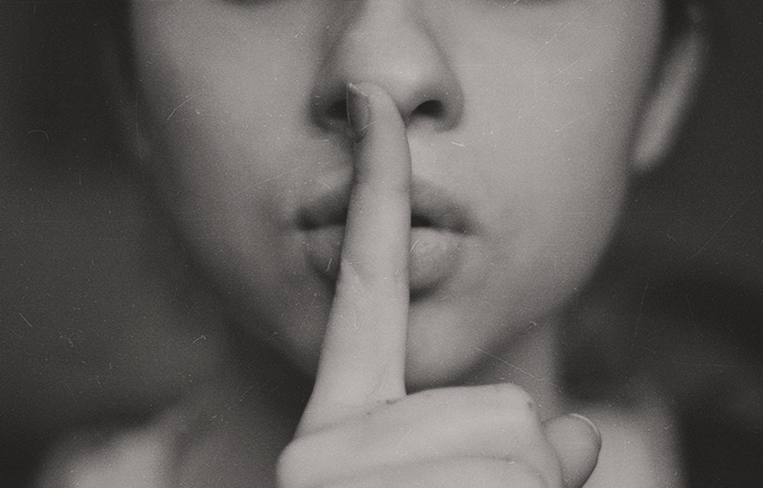 A black-and-white shot of a woman putting a finger over her lips in a gesture of silence