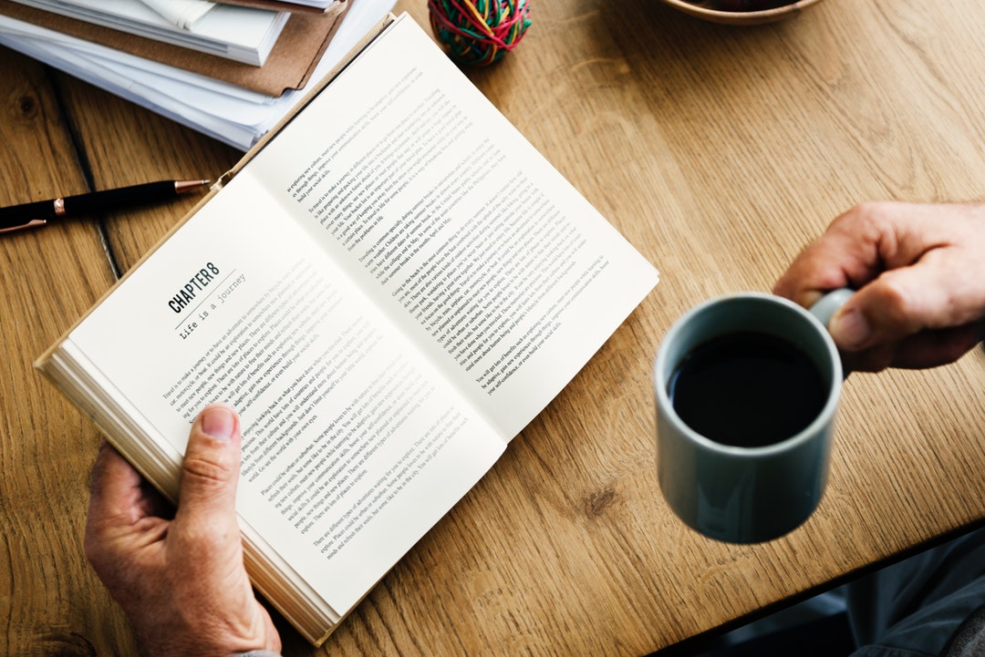 A man reads a book at a cafe in Bangkok while drinking coffee out of a mug