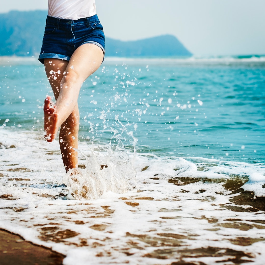 A girl wearing jean shorts splashing her feet in the ocean