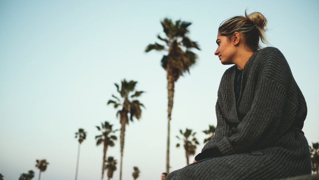 Woman in knitted cardigan sitting by the palm tree boulevard at Ocean Beach Pier
