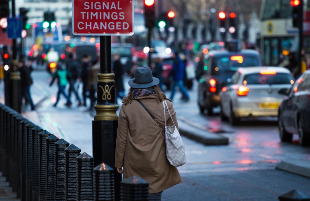 woman walking on sidewalk near red and white signal thing changed road signage