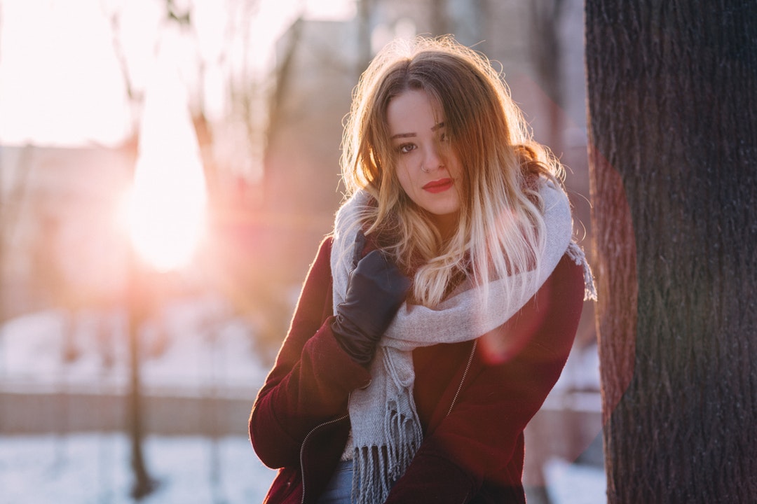 Woman in a winter sweater and fall scarf smiling near a tree outside