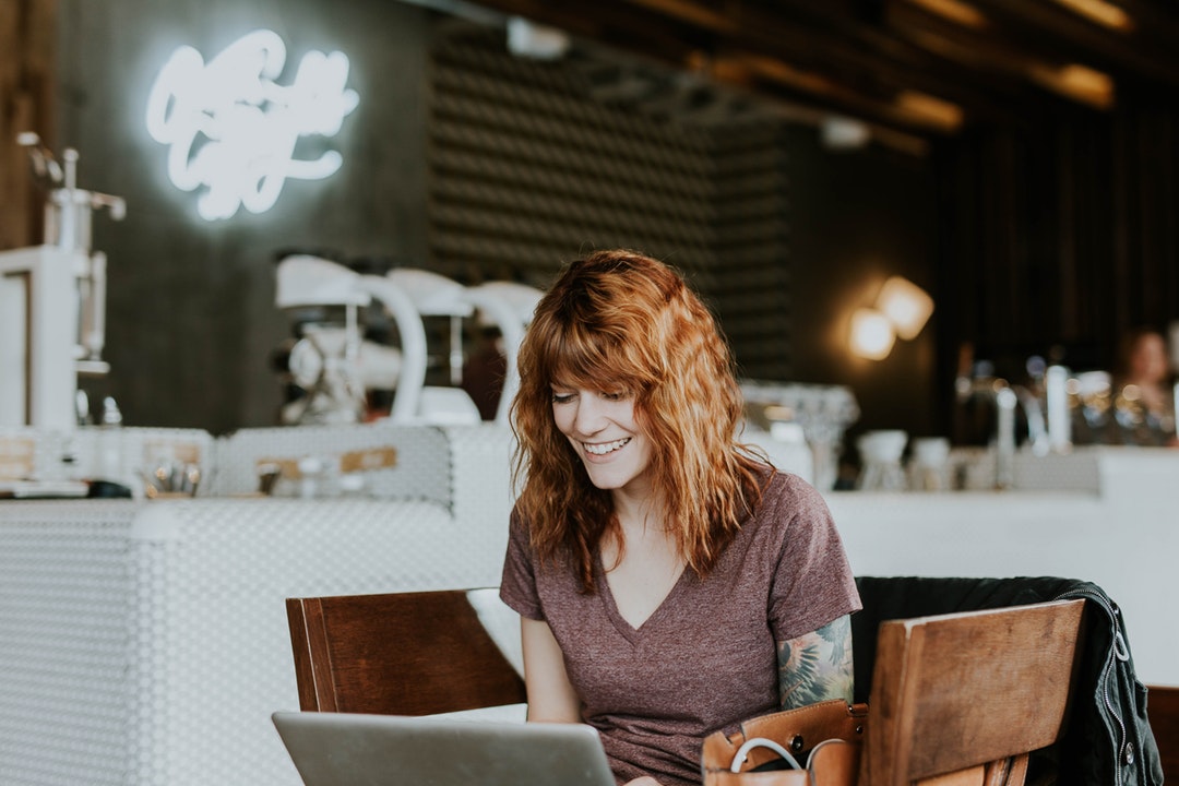 A young woman smiling while looking at a laptop screen at a coffee shop