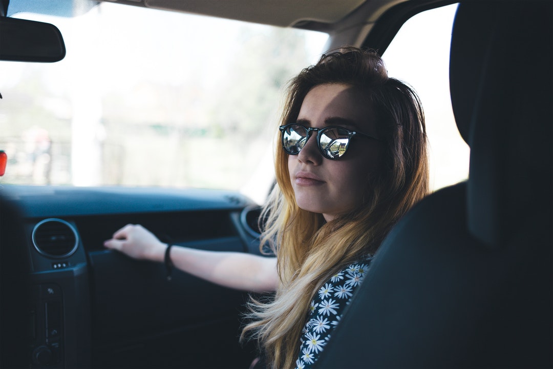 A passenger in a car wearing sunglasses touches the dashboard