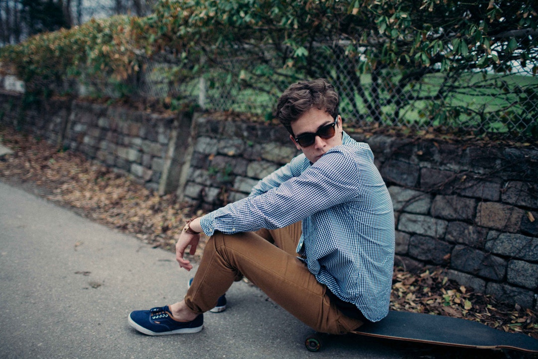 A man sitting on a skateboard wearing sunglasses