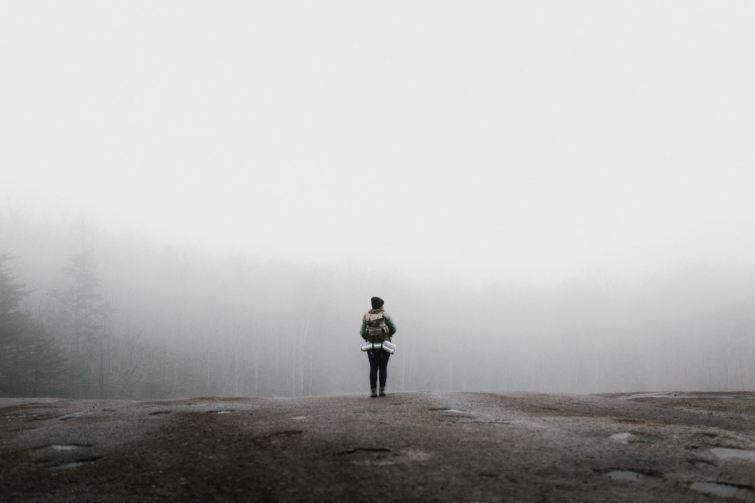 A woman standing on a rock, wearing a backpack with her gear in it, in the fog at Stone Mountain State Park