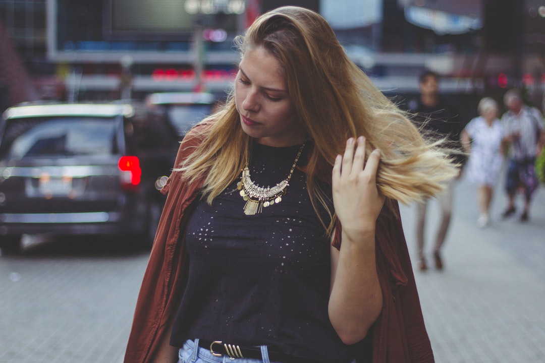 Woman in business casual wear fixes her hair while walking through the city
