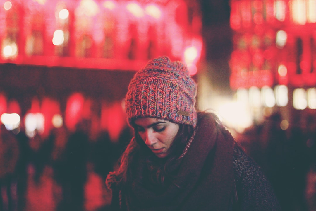 A woman in a knit cap looks down against red lights at the Grand Palace