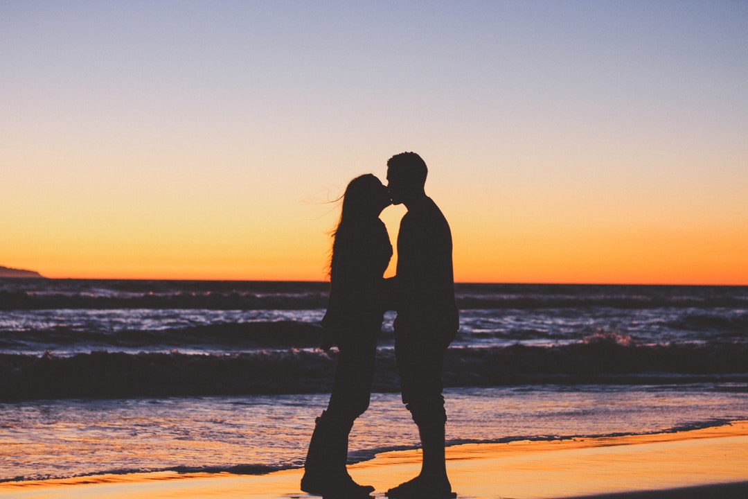 Girlfriend and boyfriend share a kiss at sunset on the beach in silhouette