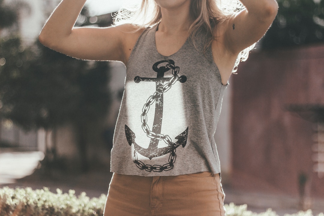 A woman in a tank top raises her arms outdoors in the sun