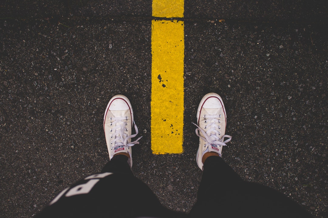A man staring down at his shoes, each on one side of the yellow street line