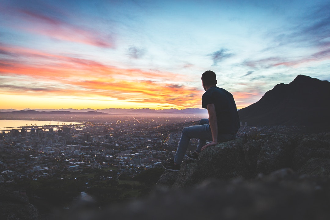 Man sitting on a rocky ledge, watching the sunset over Cape Town