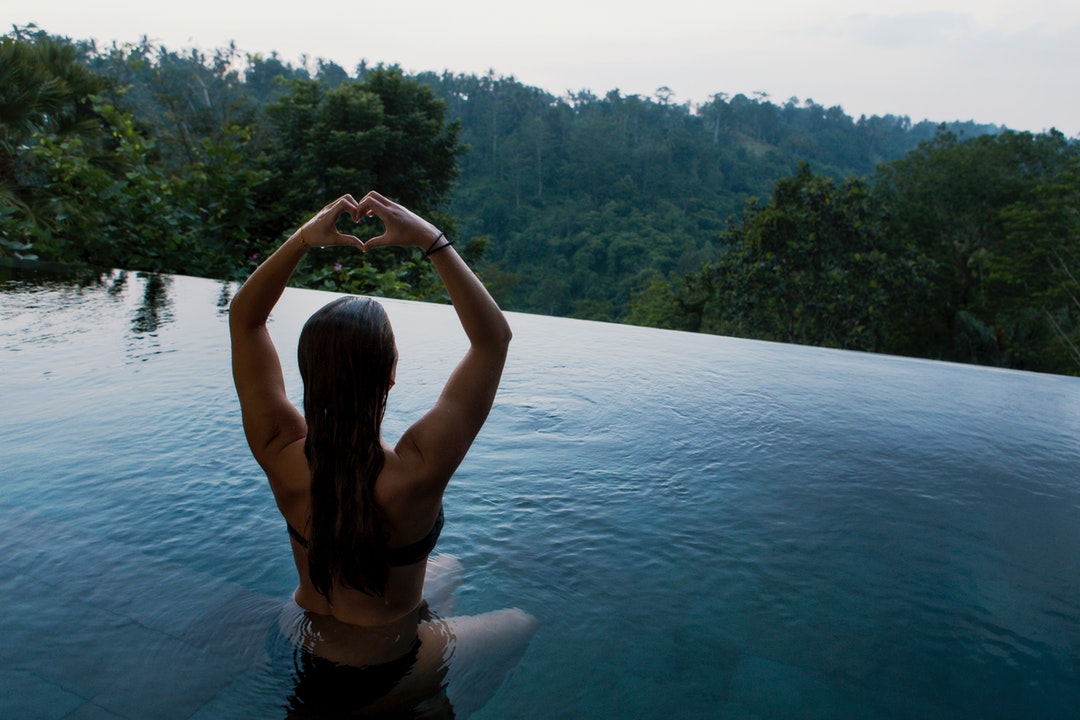 A woman meditating in an infinity pool overlooking a forest.