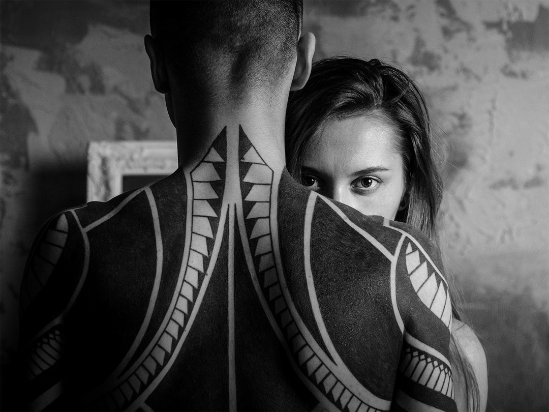 Two people face one another. The person facing away has a large back tattoo