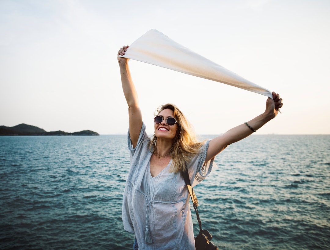 A woman wearing sunglasses holding up a white flag by the sea