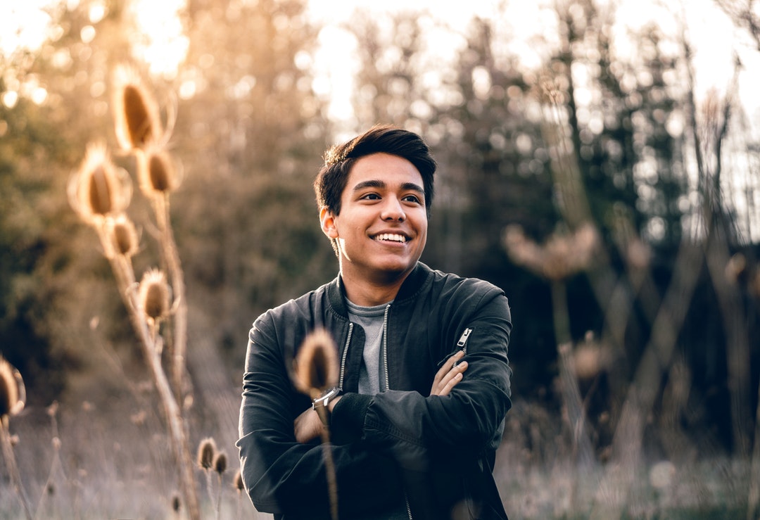 A portrait of a smiling man with crossed arms in a grassy, sunlit field