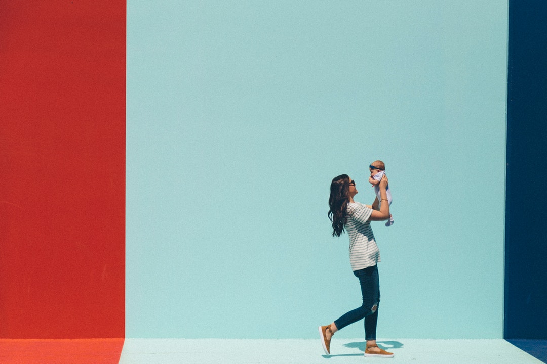 Young woman holds up her baby against backdrop of French flag mural