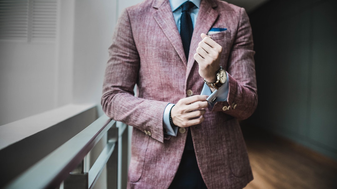 A man in a formal suit adjusting the cuffs of his shirt