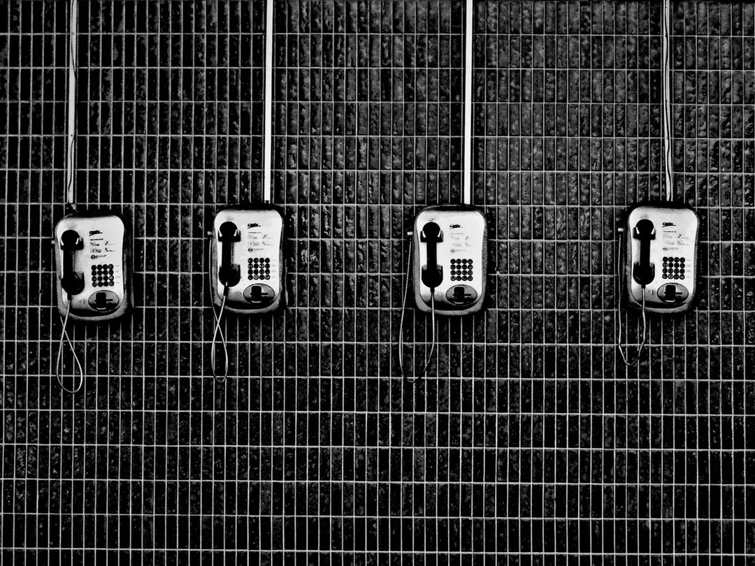 Black and white shot of four payphones on dark tiled wall