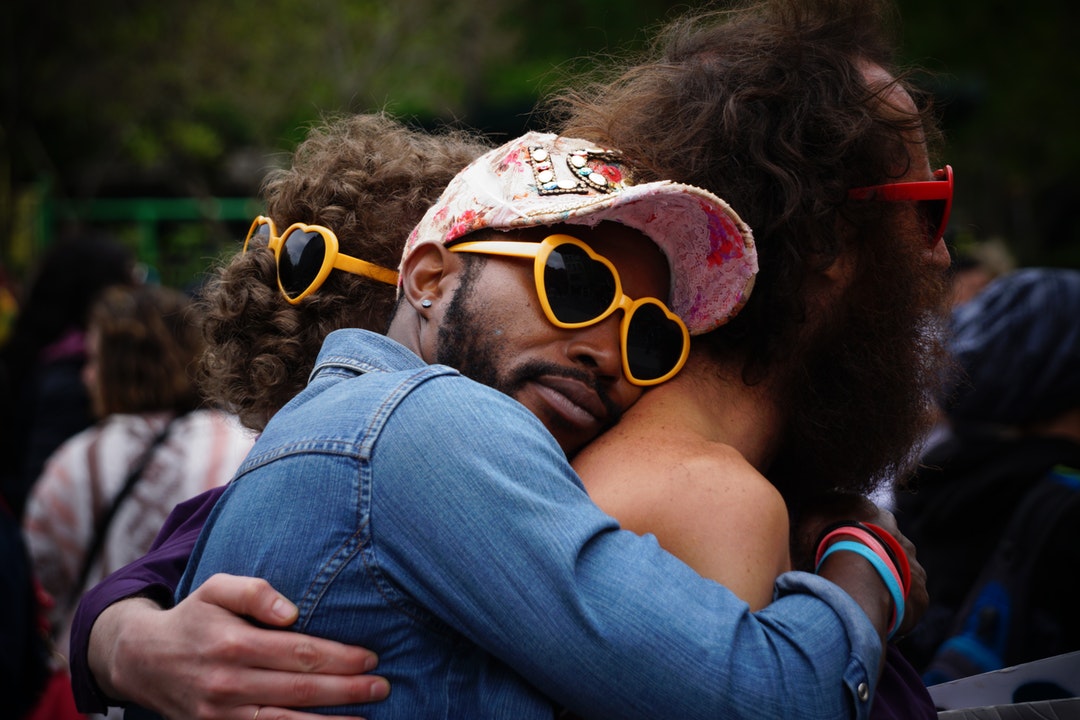 Group hug between men of different races wearing heart-shaped sunglasses