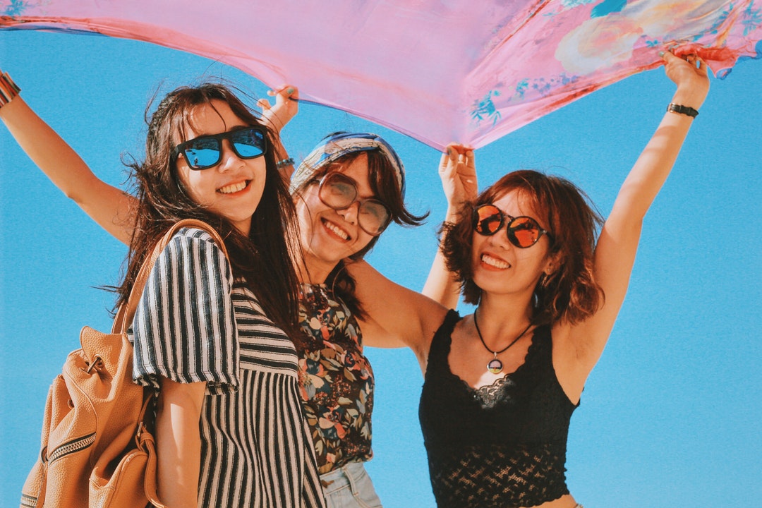 Three smiling women in glasses hold up a large pink scarf in Lý Sơn