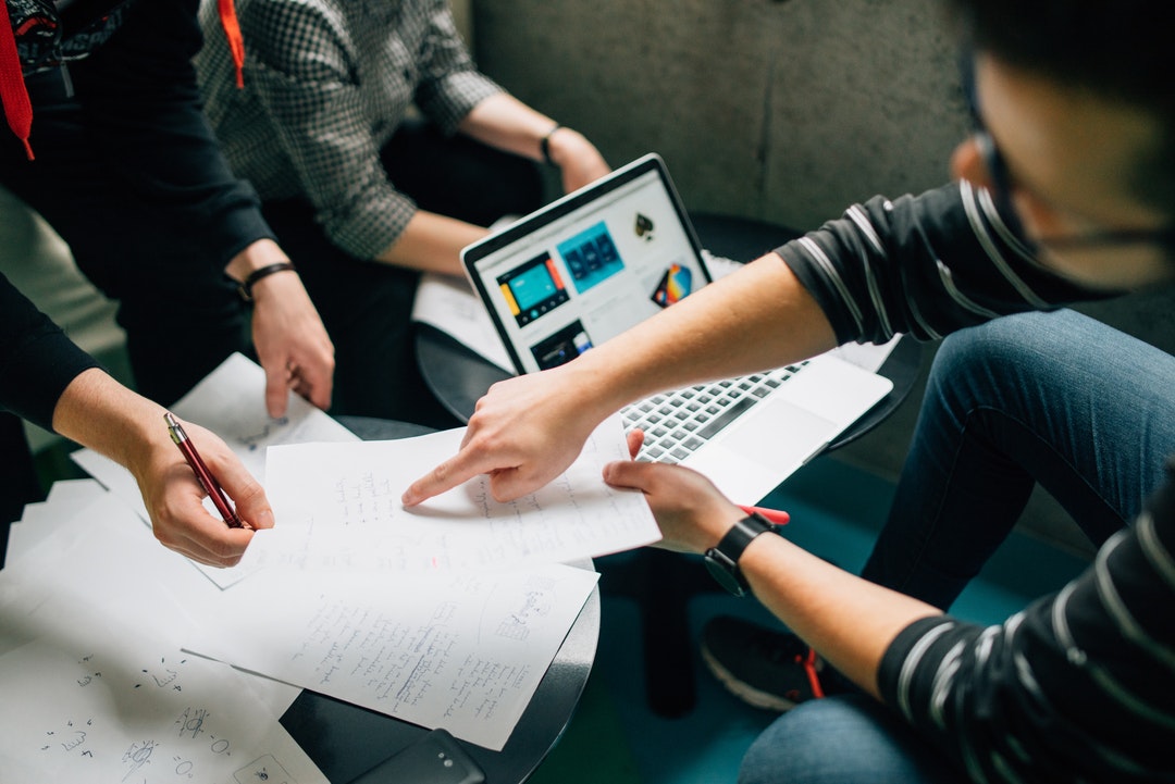 A group of people brainstorming over a laptop and sheets of paper