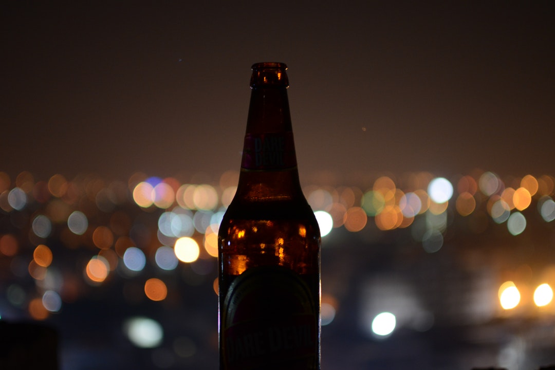Macro view of a brown dare devil beer bottle in silhouette with blurry city lights behind it