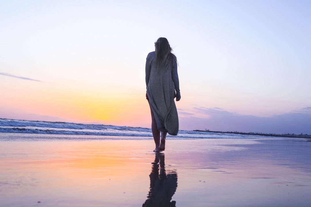 Woman walking on a wet sand beach towards the sunset at Newport Beach