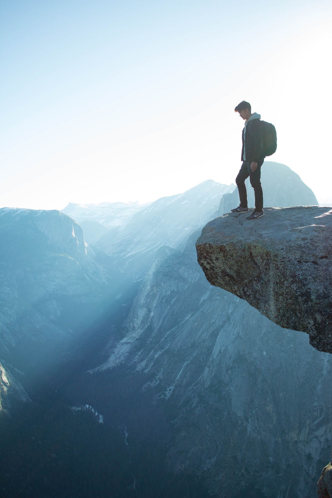 A man with a backpack approaching the edge of a ledge over a precipice