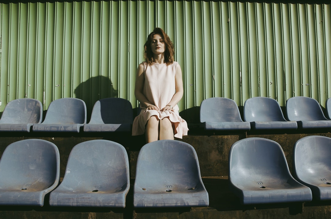 A woman in a dress sits in a row of chairs before a green wall