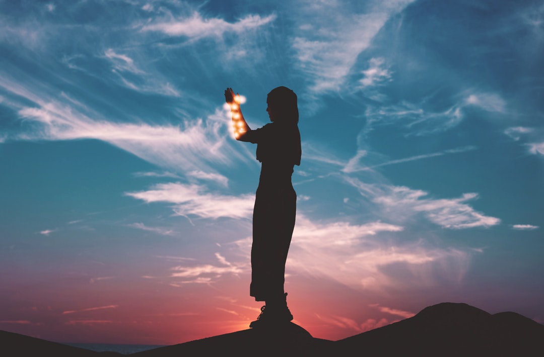 A silhouette woman holding lights stands in front of a blue and red twilight sky backdrop