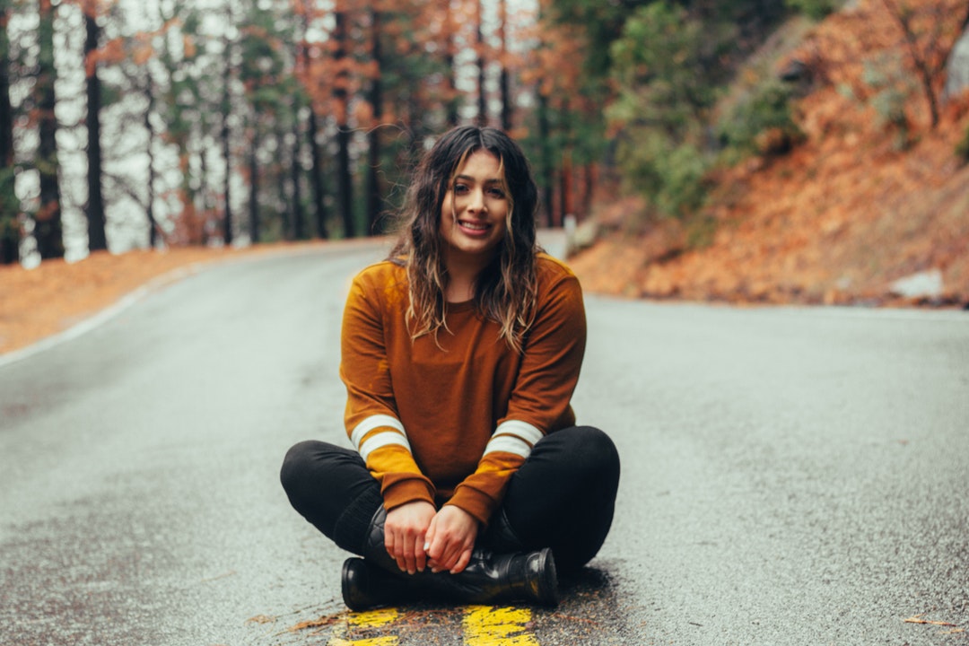 A woman with wavy hair smiles while sitting cross-legged on a road in Yosemite National Forest