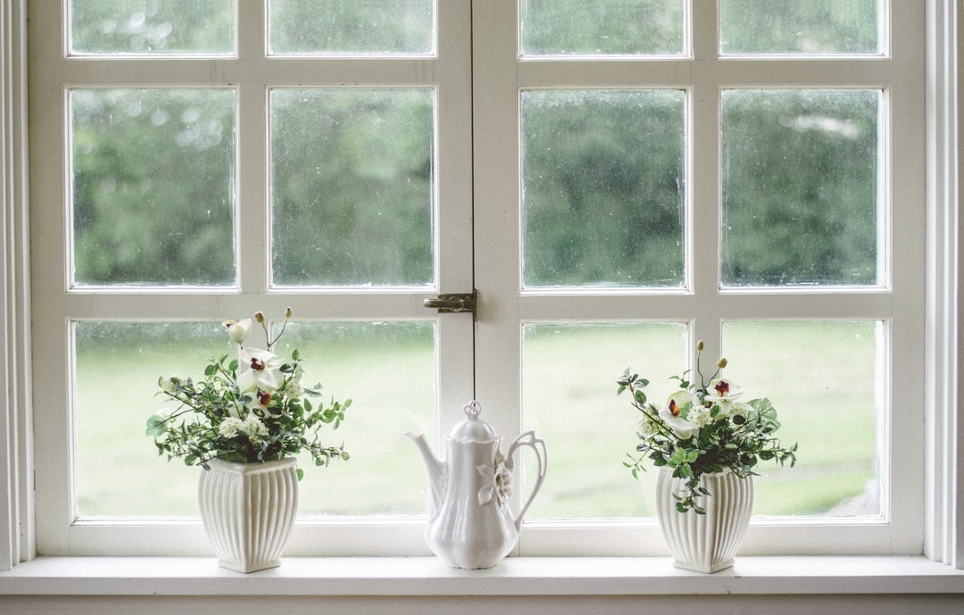 A porcelain teapot between two potted plants on a windowsill