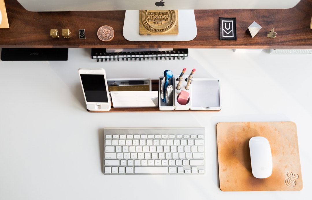 An overhead shot of a tray with an iPhone and office supplies on a computer desk