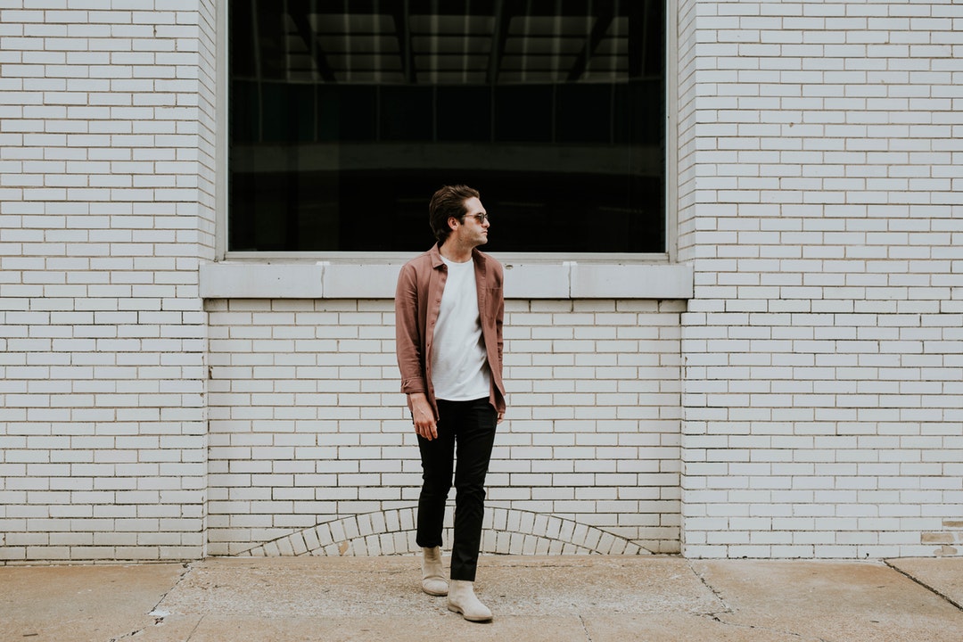 A man wearing sunglasses looks to the side in front of a white brick wall