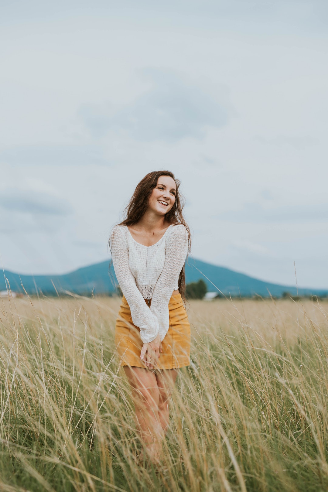 A woman wearing a skirt and long sleeve shirt standing in a field laughing