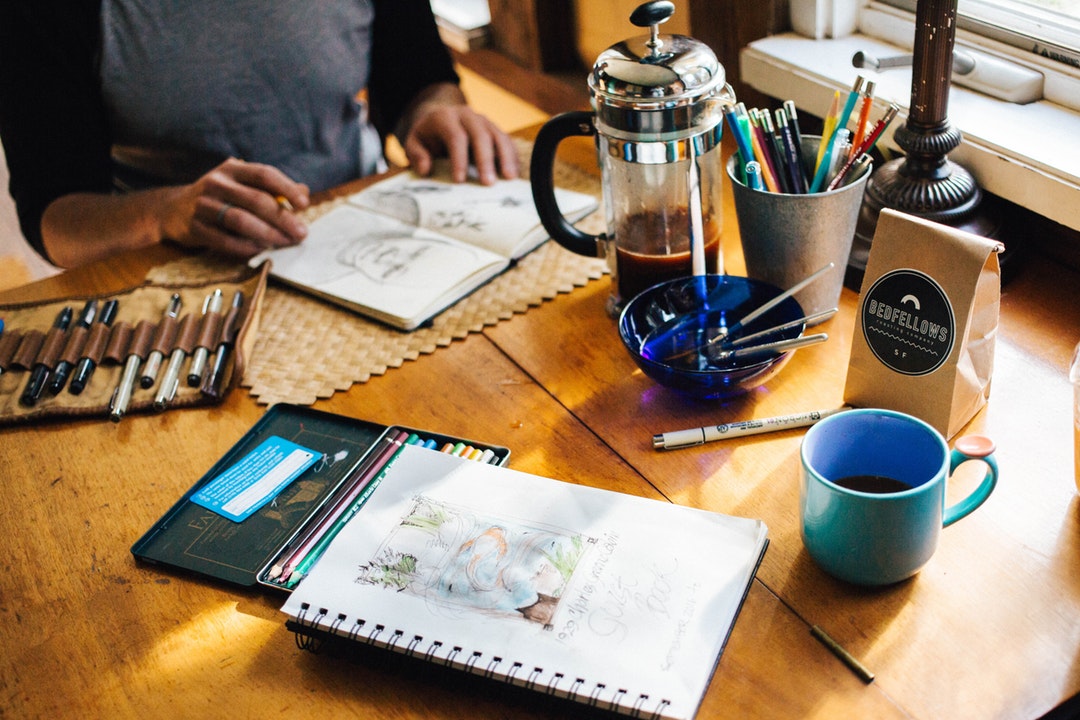 A man looking at sketches in a notebook at a table with a cup of coffee