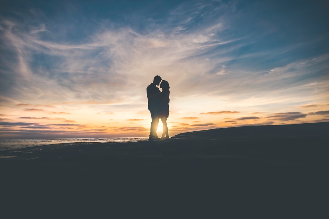 Beach scene of a young couple silhouetted against a sunset sky