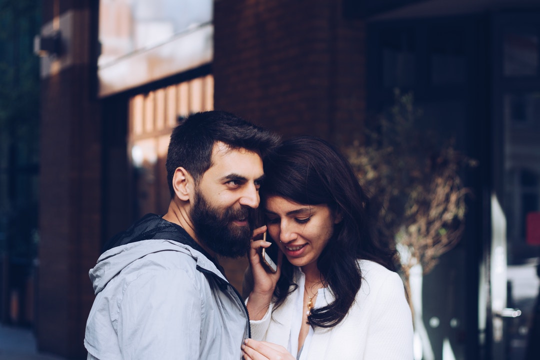 A couple stands closely outdoors in Covent Garden while the woman talks on an iPhone