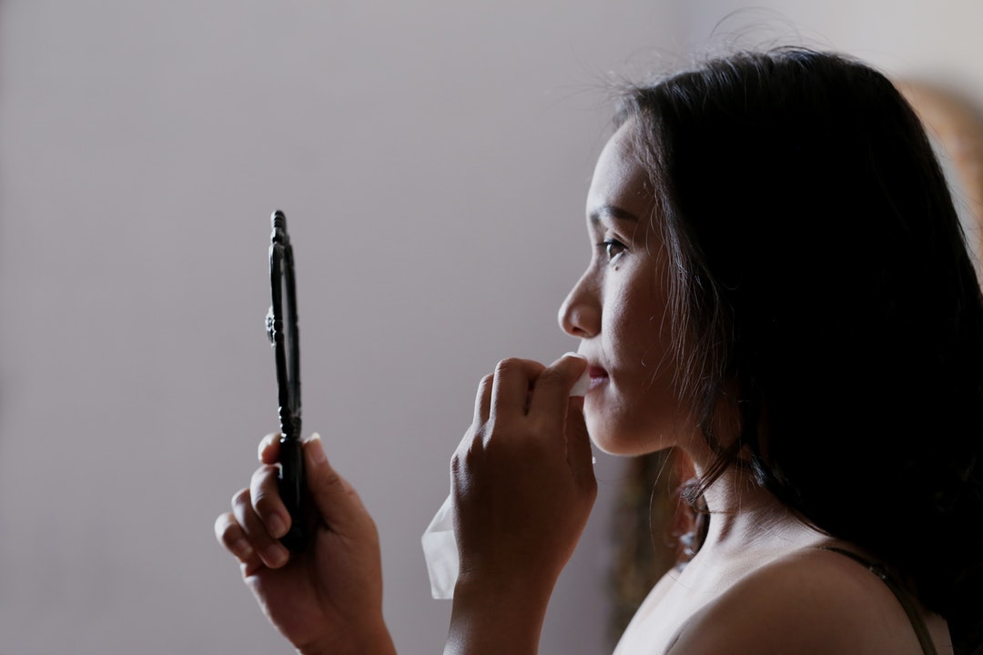 A woman dabs her mouth with a napkin while holding a hand mirror in Bekasi.