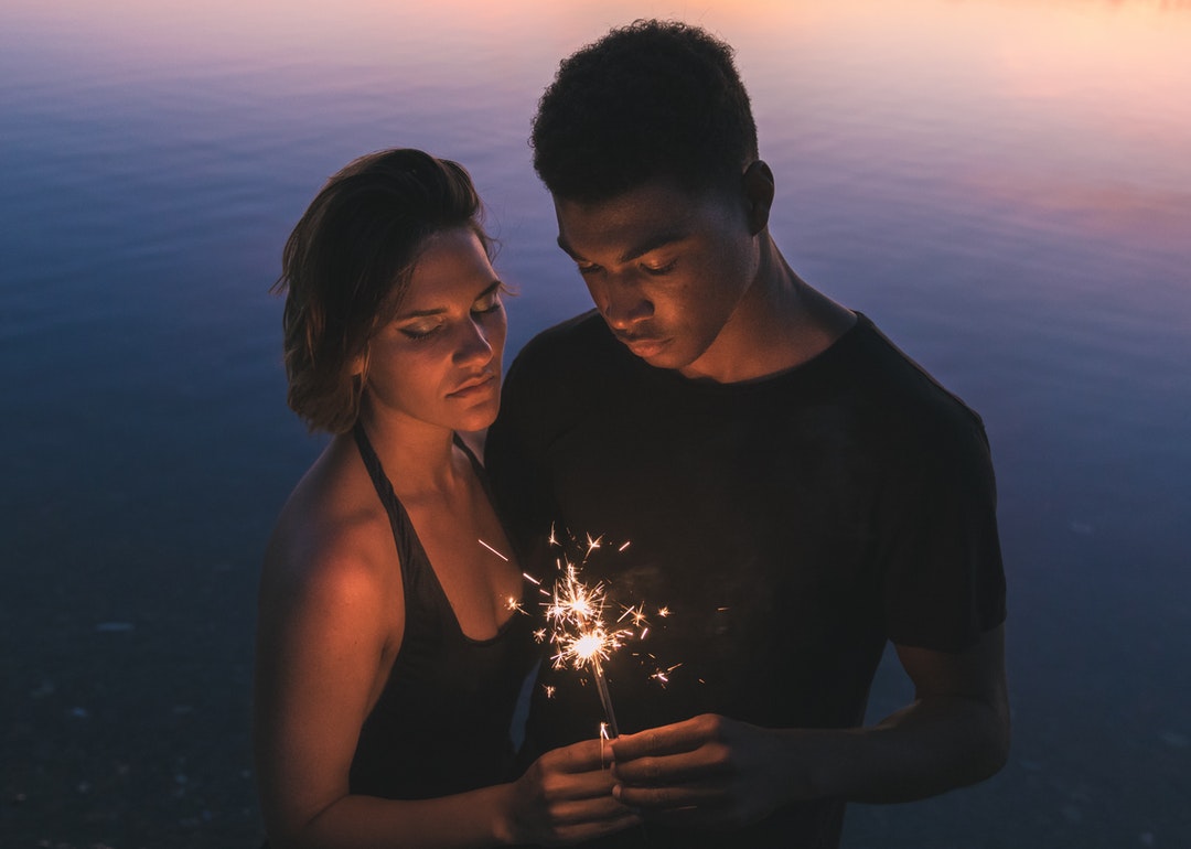 Couple with closed eyes holding a sparkler at twilight