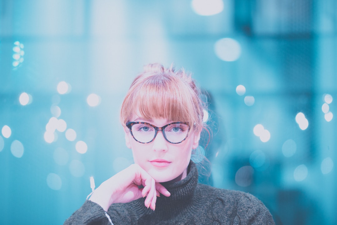 A young blonde woman in glasses against a blue background