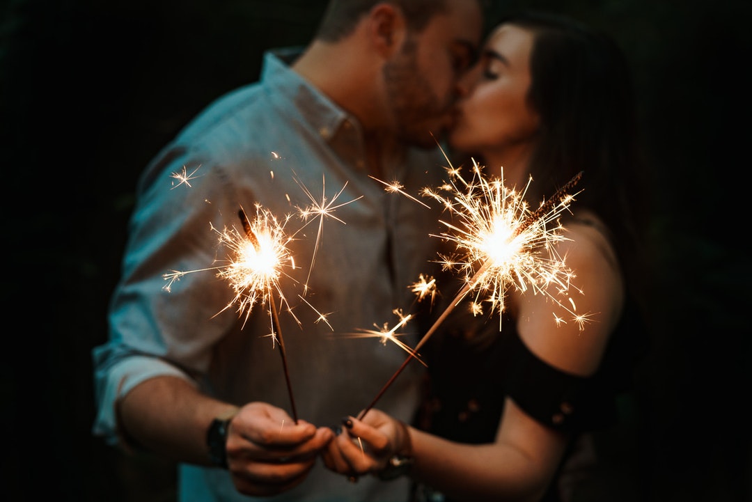 man and woman kissing each other while holding fireworks low-light photography