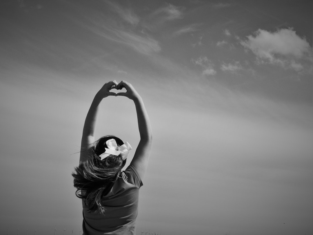 A black-and-white shot of a woman holding up her hands and forming a heart shape with her fingers