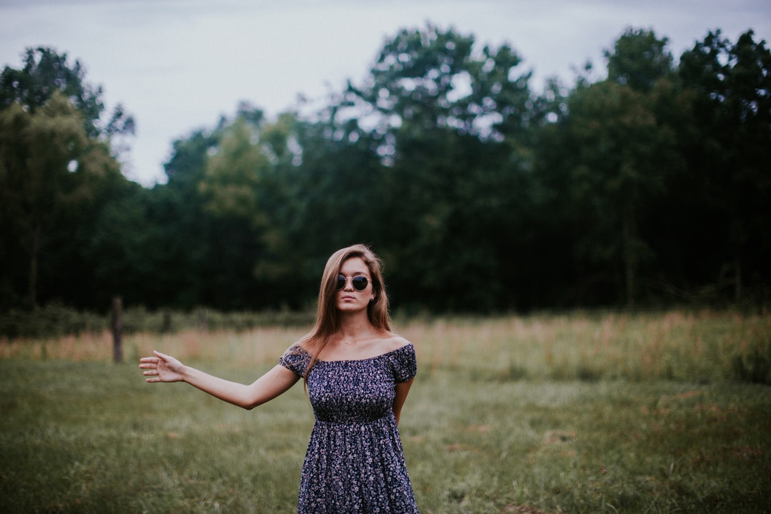 Woman in a dress standing in a field with her arm outstretched