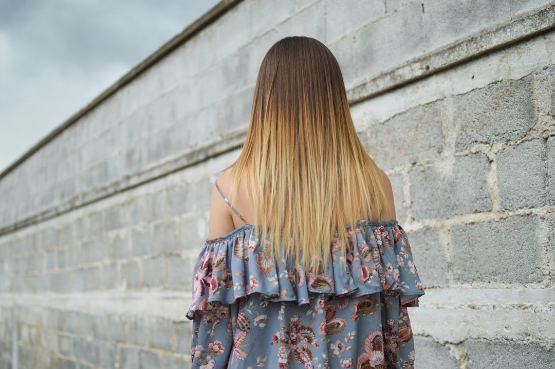 Brunette woman with blonde highlights a blue floral dress beside a stone wall under a gray sky