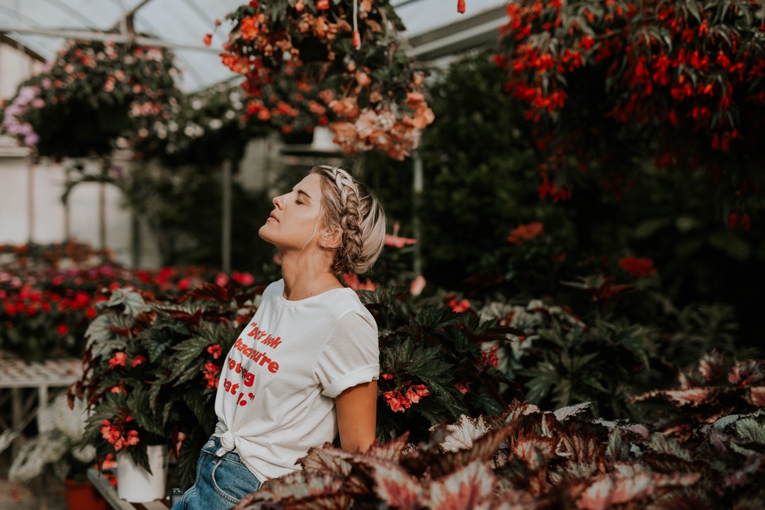 A woman with a braid closes her eyes with her head back in a botanical garden