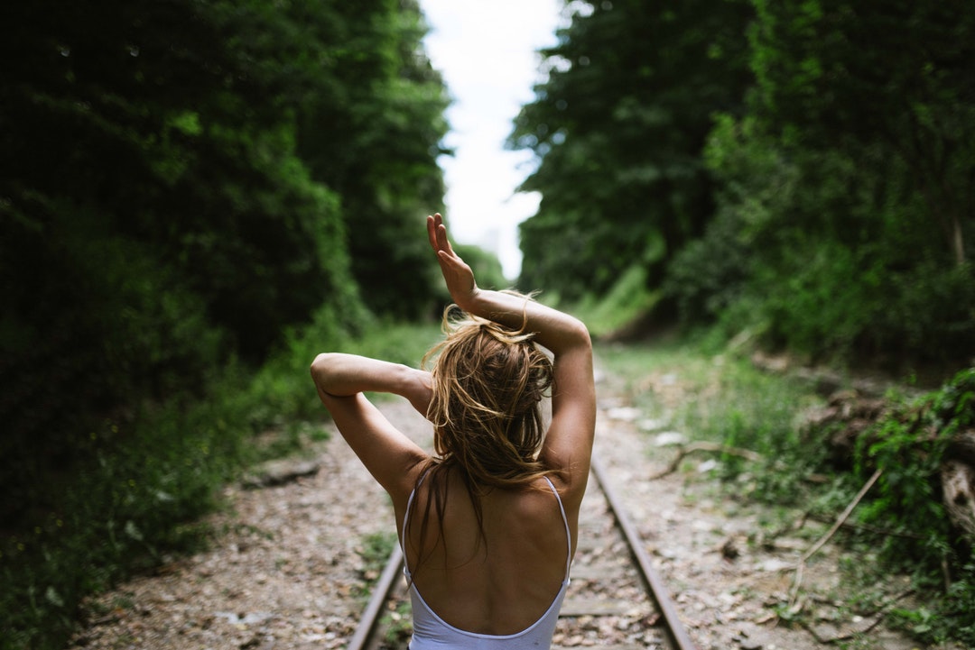 A woman faces away down outdoor train tracks in Paris with her arms over her head